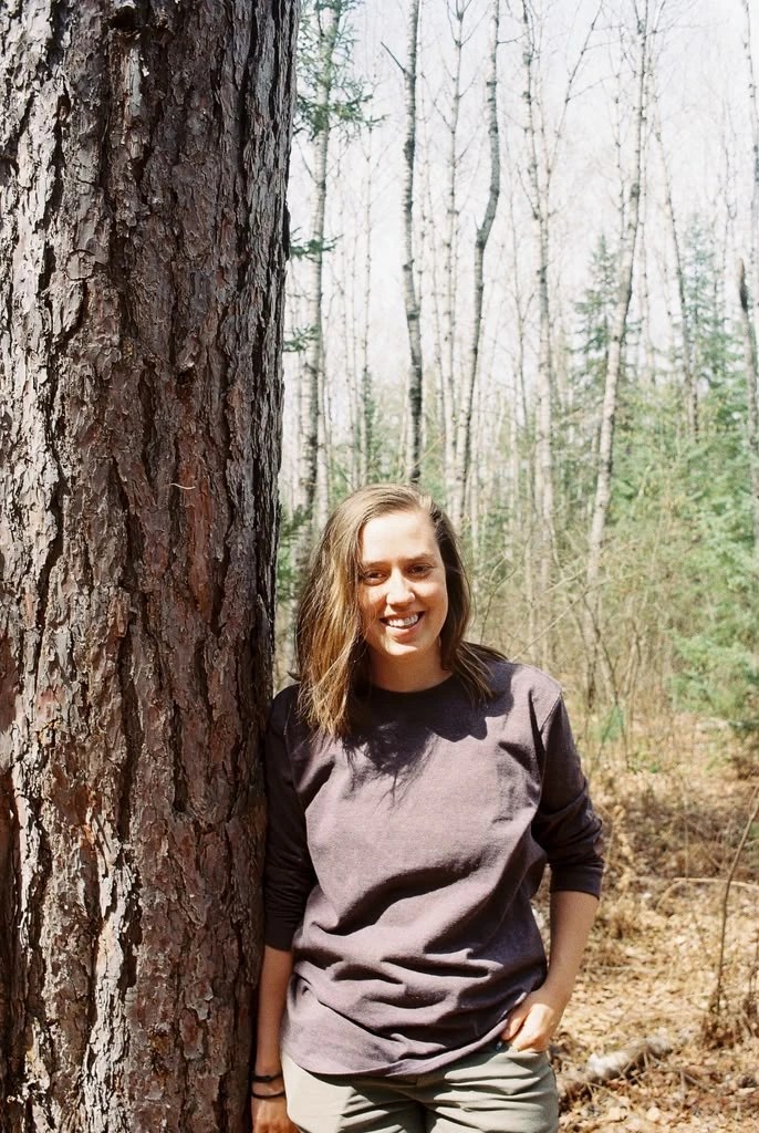 Carlie Haben standing beside a large pine tree